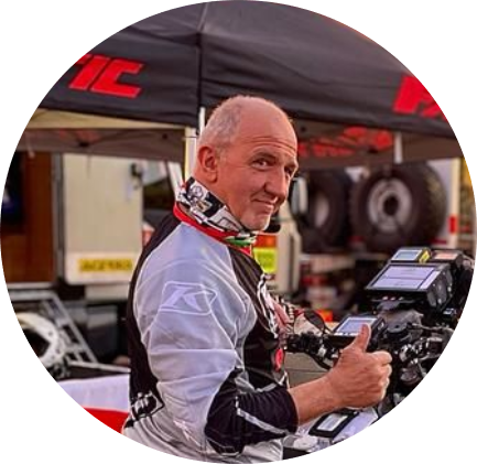 En man i racingkläder ger tummen upp framför ett tält och motorcyklar.