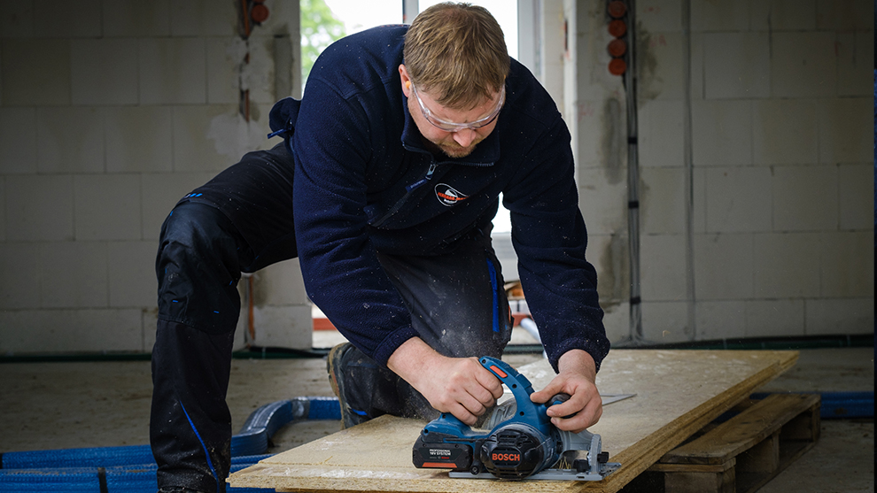 Mees kaitseprillidega lõikab puitu sinise Bosch saega.