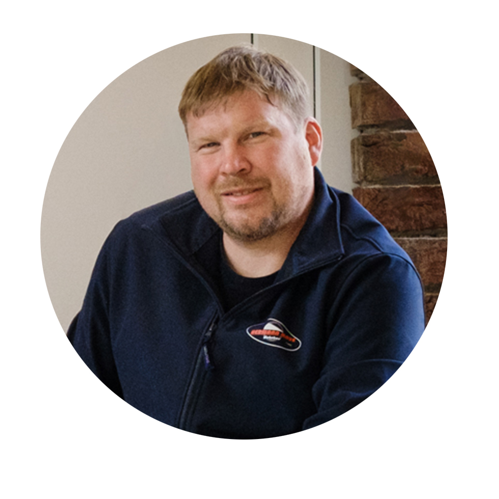 Lühikese juustega mees naeratab sinises jakis seina ees.