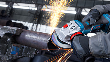 Een hand houdt een haakse slijper tegen een metalen buis, vonken spatten tijdens het snijden.