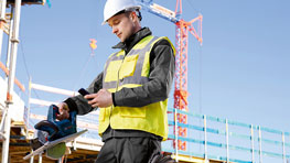 Ein Bauarbeiter in gelb-grüner Weste nutzt ein Werkzeug auf der Baustelle.