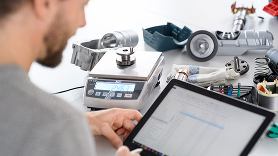 En man väger verktyg på en digital våg och använder en surfplatta.