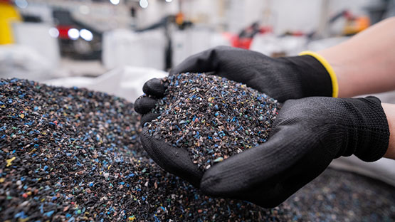 Händer med svarta handskar håller färgglada plastgranulat.