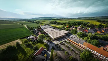 Luftfoto av en stor byggnad omgiven av fält och bostadshus.