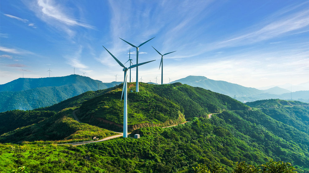 Vindkraftverk står på gröna kullar under en blå himmel.