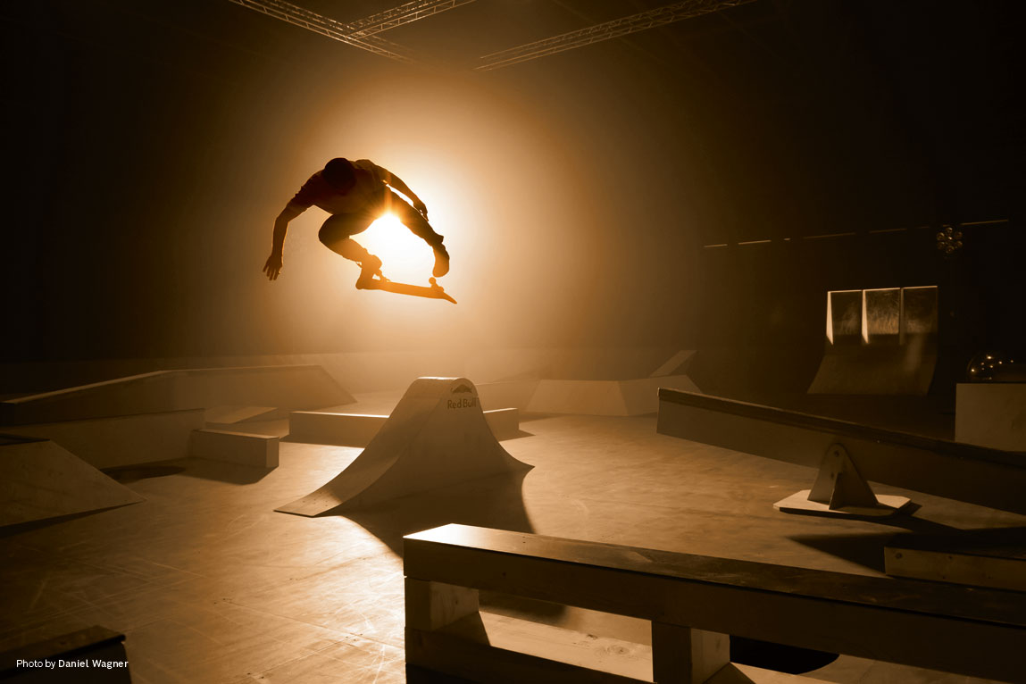 Ένας σκέιτερ πηδά πάνω από ράμπες σε αμυδρό φως.