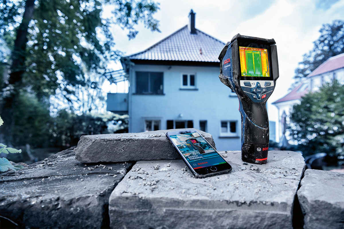 Тепловизор Bosch Professional стоит на камнях рядом со смартфоном.