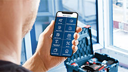 En man håller en smartphone med en app i handen, resväska i bakgrunden.