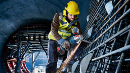Ein Arbeiter mit gelbem Helm und Warnweste schneidet Metallstäbe.