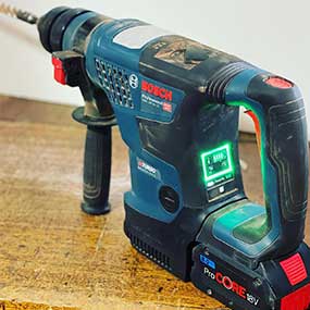 A blue Bosch Professional cordless hammer drill stands on a wooden surface.