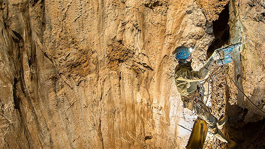 Pracownik w odzieży ochronnej i kasku używa wiertarki Bosch Professional, wisząc na ścianie skalnej.