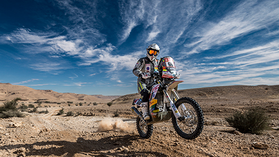 A motorcyclist jumps over a sandy surface in the desert.