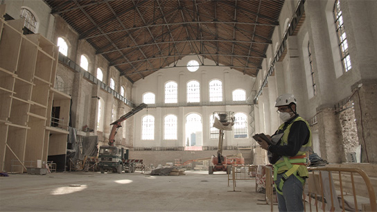 Byggarbetsplats med arbetare i säkerhetskläder, höga fönster och ställningar.