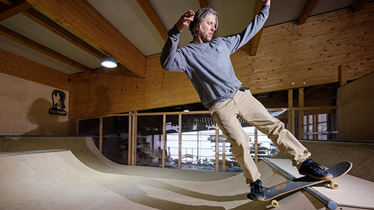 A skater in a gray sweater is skating on a wooden ramp.