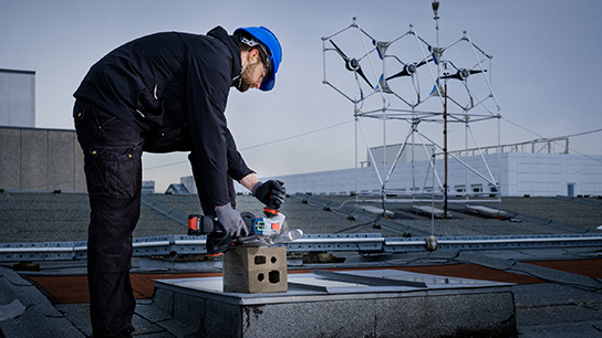 A worker with a blue helmet is using a Bosch tool on a roof.