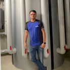 Mann in blauer Shirt lehnt an großen, grauen Rohren in einer Fabrik.