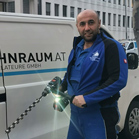 Ein Handwerker in blauer Arbeitskleidung hält eine Bohrmaschine neben einem Van.