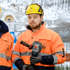 Zwei Arbeiter in orangefarbener Schutzkleidung stehen in verschneiter Landschaft.