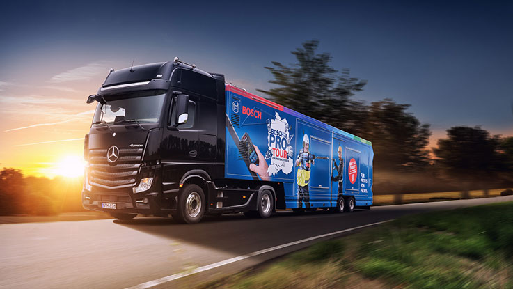 Schwarzer Mercedes-Lkw mit blauem Bosch-Werbeaufdruck fährt auf Straße.