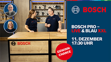 Zwei Personen stehen an einem Holzarbeitsplatz, umgeben von Werkzeugen. Sie diskutieren mit freundlichen Gesichtsausdrücken.