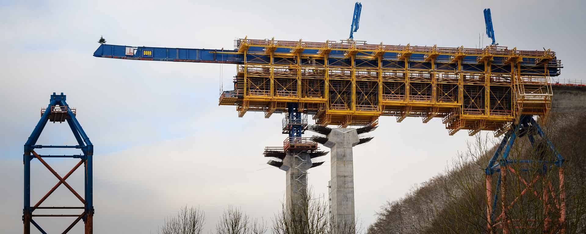 A large yellow structure rises above blue steel beams.