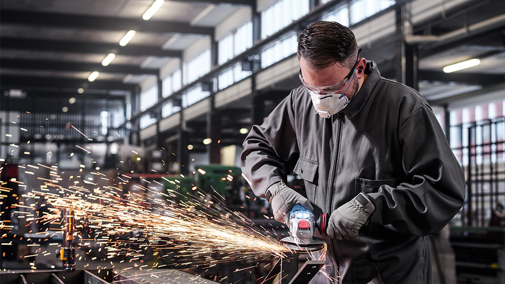 A man with safety glasses is cutting metal, sparks are flying.