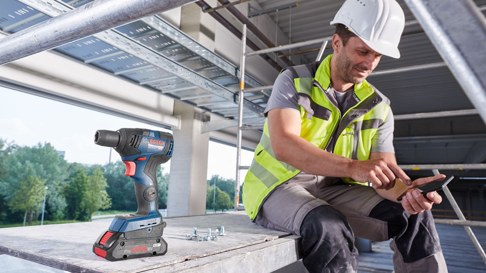 Аккумуляторная отвертка Bosch Professional на строительной площадке, рабочий использует смартфон.