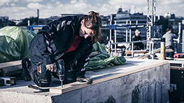 En kvinna i arbetskläder borrar med en batteridriven skruvdragare på en byggarbetsplats.