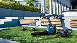 Trois outils Bosch Professional sont posés sur de l'herbe verte, entourés de bancs.