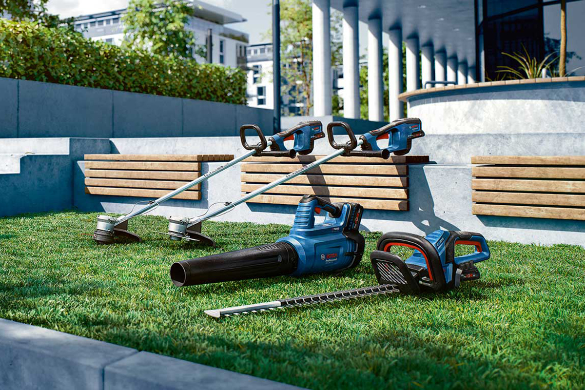 Tři profesionální zahradnické nástroje Bosch leží na zelené trávě.