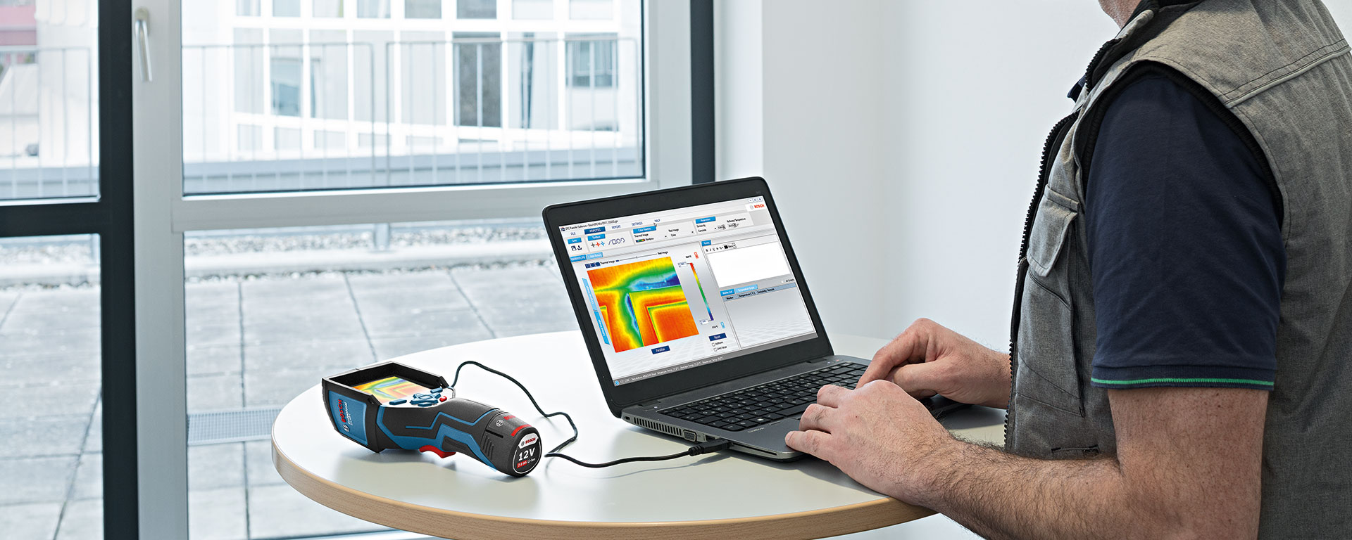 A person uses a laptop connected to a Bosch thermal camera on a table.
