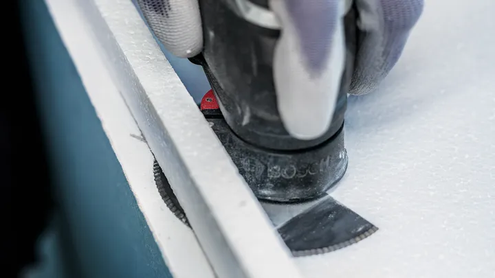 يقوم الشخص الذي يرتدي معدات السلامة بقطع لوحة خشبية باستخدام شفرة متعددة الأدوات.