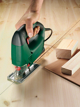 A worker guides a jigsaw along a marked line cutting plywood.