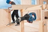 A person wearing safety equipment constructs a wooden frame near a cordless reciprocating saw.