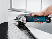 A person uses a cordless universal shear to cut textured rubber flooring.