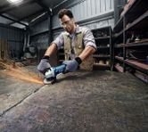 A person wearing safety equipment grinds a metal surface with an angle grinder.