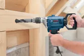A person operates a power drill to bore a hole through a wooden beam.