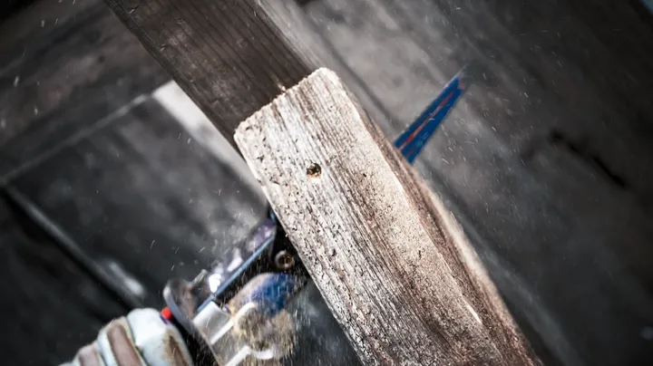 Person wearing safety equipment cuts a wooden plank with a reciprocating saw.