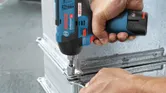 Person using a cordless impact wrench to fasten a bolt onto a metal frame.
