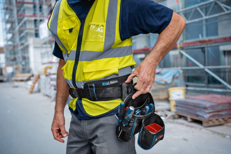 Person wearing safety equipment adjusts a tool belt at a construction site.