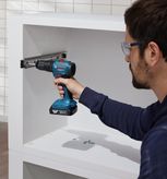 A person wearing safety equipment uses a cordless drill to install a cabinet rail.