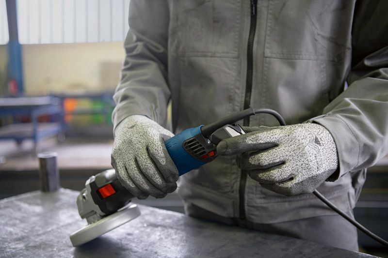 A person wearing safety equipment prepares to plug in an angle grinder.