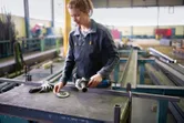 A person wearing safety equipment prepares an angle grinder on a metal workbench.