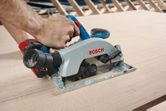 Person operates a cordless circular saw cutting wood on a construction site.