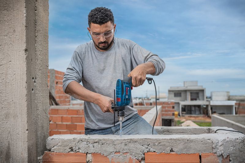 A person wearing safety equipment drills into a concrete wall at a construction site.