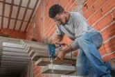 A person wearing safety equipment drills into a concrete staircase with an impact drill.