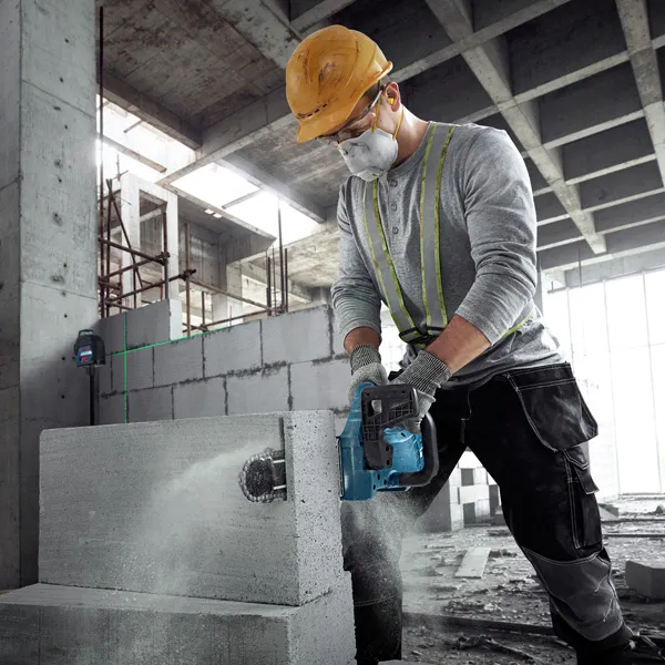 A person wearing safety equipment cuts an AAC block using a power cutter.