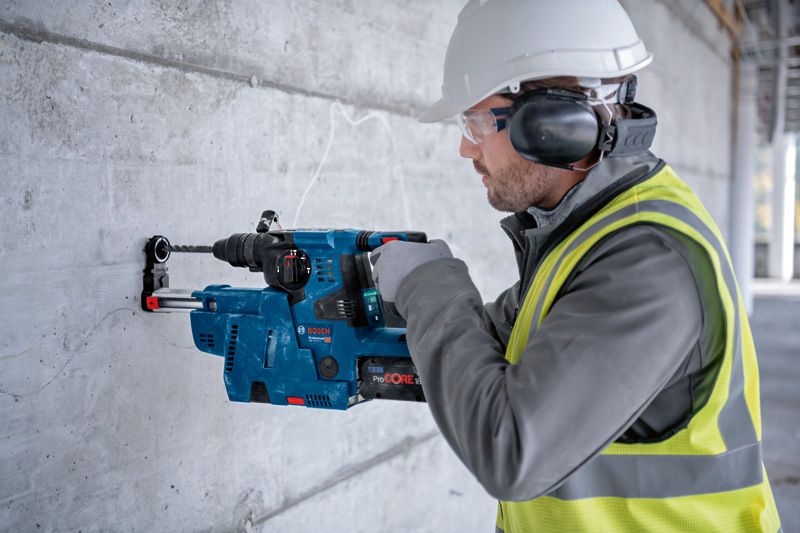Person wearing safety equipment drills into a concrete wall using a rotary hammer.