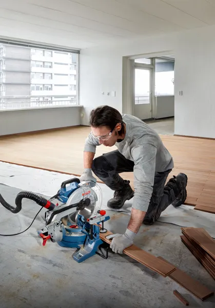A person wearing safety equipment cuts wooden flooring with a mitre saw.