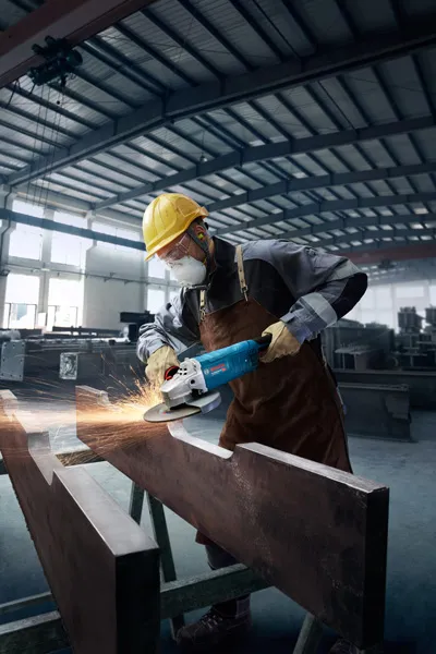 A person wearing safety equipment grinds a metal beam in an industrial workshop.
